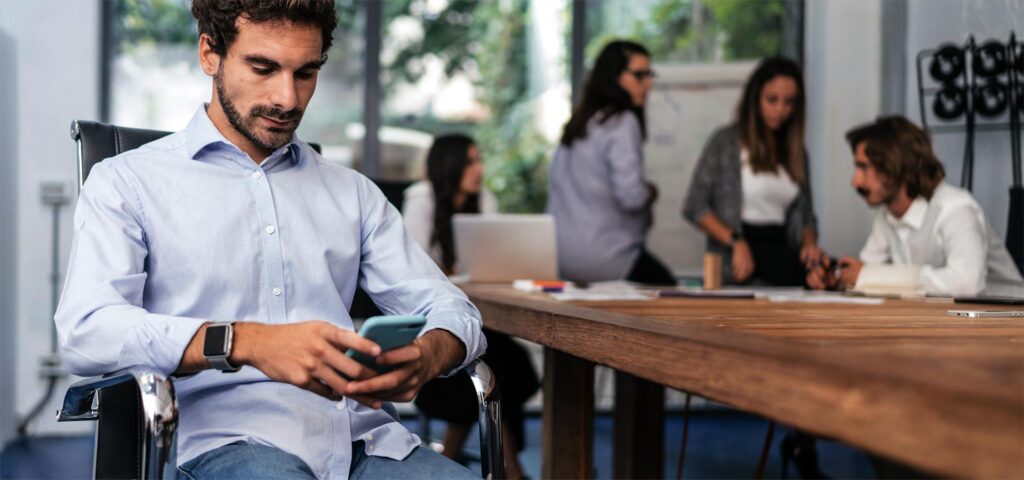 A group of people, in the foreground a man using a smartphone.