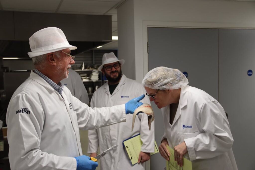 Trainer holding a piece of fish being smelt by a trainee with another trainee looking on