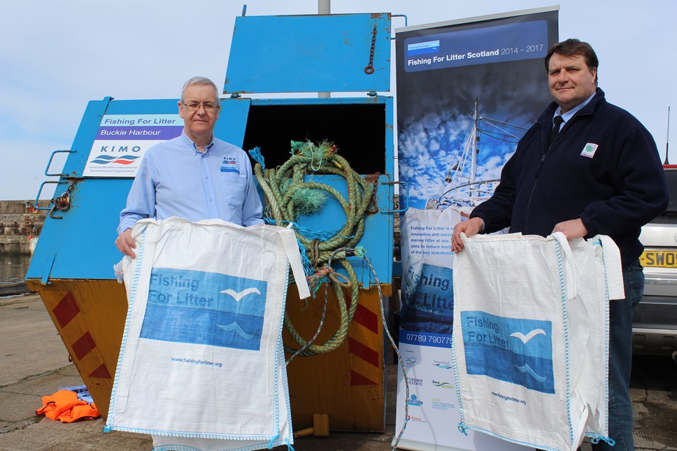 2 men hold marine litter bags in front of waste skips