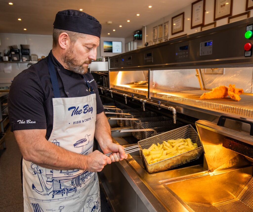 Fish frier holding a basket of chips over a frying range