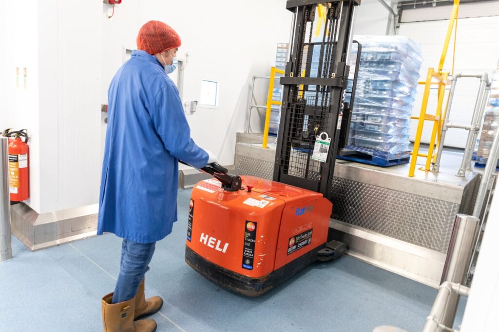A man in food factory clothing operating a powered hand forklift